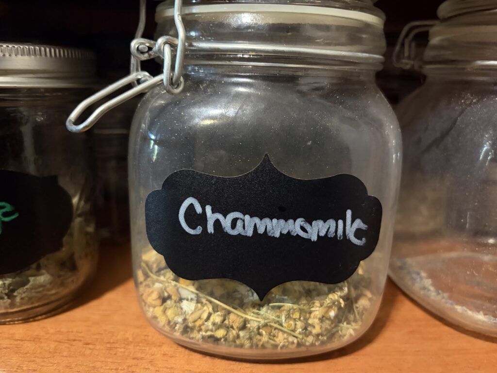 Airtight jar with chamomile label sits on pantry shelf with dried chamomile flowers inside