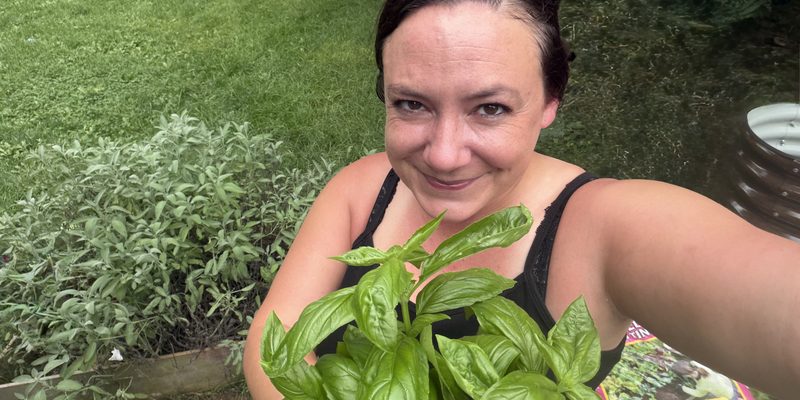 woman smiling holding basil in front of garden bed